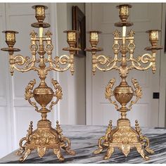 two golden candelabra stands on a marble table