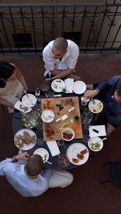 four people sitting at a table with plates of food in front of them, looking down