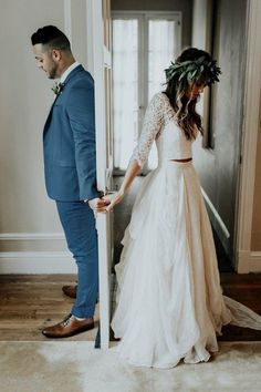 a man and woman standing next to each other in front of an open door wearing wedding dresses