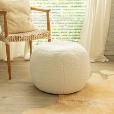 a white round ottoman sitting on top of a hard wood floor next to a window