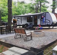 an rv parked in the woods next to a fire pit and picnic table with chairs