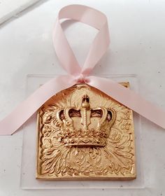 a gold ornament with a pink ribbon around it and a crown on top