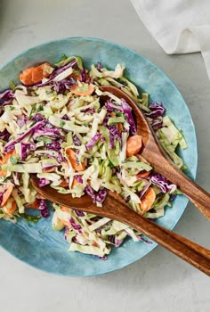 a bowl filled with coleslaw and carrots next to a wooden spoon