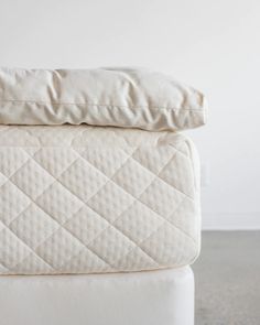 two mattresses stacked on top of each other, one with white sheets and the other without