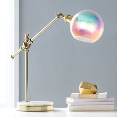 a desk lamp that is on top of a table next to books and a glass ball