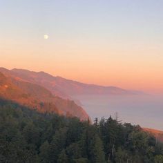 the sun is setting over mountains with trees on each side and fog in the air