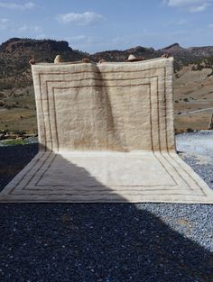 a large rug sitting on top of gravel covered ground next to mountains and sky in the background