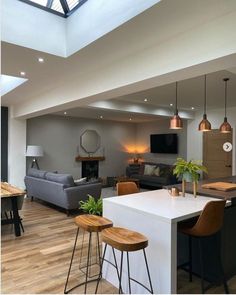 an open concept living and dining room with wood flooring, white walls, gray couches, black bar stools