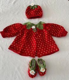 a red knitted doll outfit and matching shoes on a white tablecloth with a pair of baby's slippers