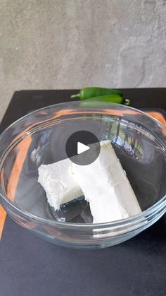 a glass bowl filled with white cheese on top of a black counter next to a green pepper