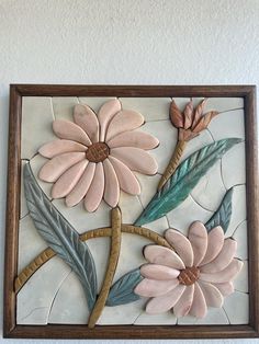 a flower made out of clay sitting on top of a white wall next to a wooden frame