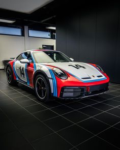 a red, white and blue sports car parked in a garage with black tile flooring