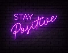 a purple neon sign that says stay positive on a brick wall in front of it