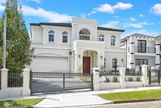 a large white house with lots of windows on it's sides and a fence around the front yard