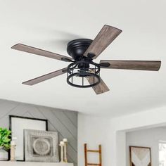 a black ceiling fan with wooden blades in a white living room, next to a fireplace