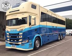 a large blue and beige bus parked in a parking lot next to a building with cars