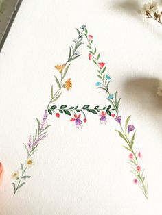 a watercolor drawing of a triangle with flowers and leaves on the side, next to a pencil