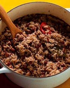 a pot filled with rice and beans on top of a yellow table cloth next to a wooden spoon