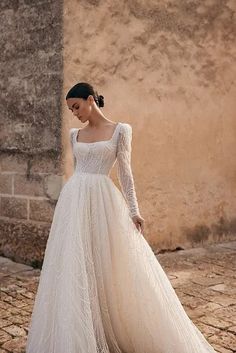 a woman in a wedding dress is standing on a cobblestone street and looking down at the ground