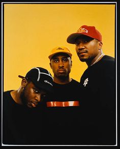 three men standing next to each other in front of a yellow background with one man wearing a red hat