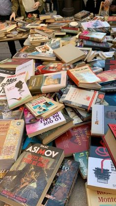 many books are laying on the ground and people are looking at them in the background