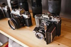 an old camera sitting on top of a wooden table next to other cameras and lenses