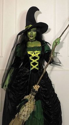 a woman dressed as a witch holding a broom and wearing a black dress with green trim