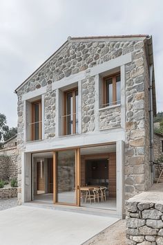 a stone building with wooden doors and windows on the outside, next to an outdoor patio