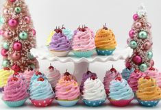 cupcakes are arranged on a cake stand with christmas trees and ornaments in the background