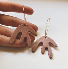 a pair of hand shaped wooden earrings on top of a white table next to a person's hand