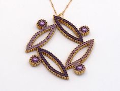 a purple and gold necklace on a white surface with an intricate design in the middle