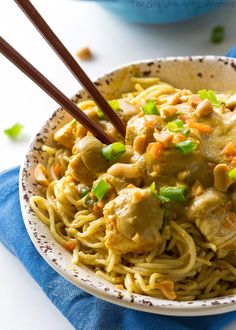 a white bowl filled with noodles and meat on top of a blue napkin next to chopsticks