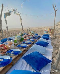 a long table set up on the beach with blue and white linens