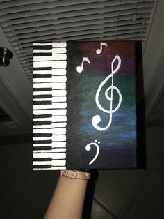 someone is holding up a book with music notes painted on it and the piano keys are white