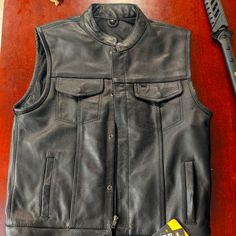 a black leather vest sitting on top of a wooden table next to a razor blade