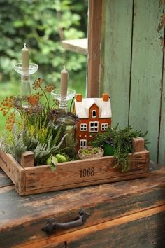 a wooden tray filled with plants and candles on top of a table next to a window