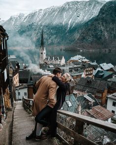 a man and woman embracing each other in front of a town with mountains behind them