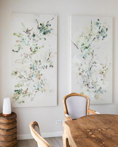 two paintings hang on the wall above a wooden table with chairs in front of it