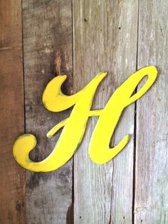 the letter h is painted yellow on a wooden wall