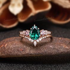 a ring with an emerald surrounded by white diamonds on top of a piece of wood