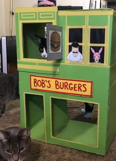 a cat is laying on the floor in front of a toy burger house with two cats