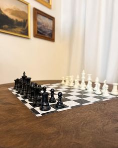 a chess board with pieces on it sitting in front of a painting and framed pictures