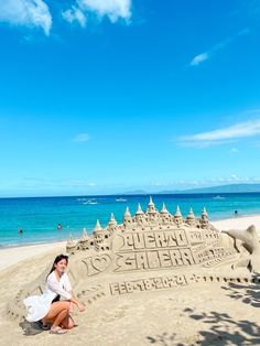 a woman sitting in front of a sand castle on the beach