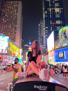 a woman sitting on top of a car in the middle of a city at night