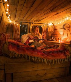 a woman sitting on top of a bed with a guitar in her lap and string lights hanging from the ceiling