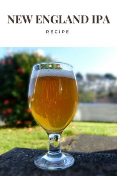 a glass of beer sitting on top of a table next to some grass and bushes