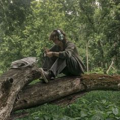 a man sitting on top of a fallen tree in the forest with headphones on