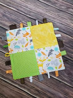 two baby bibs are laying next to each other on a wooden surface, one is yellow and the other is green