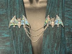 A set of flying bats with mother of pearl inlays set in silver.  Sweater pins and clips were very popular in the 1950s and are very much making a comeback today with the trend in retro wear.  These bats already have brooch style pins on the back, but you can choose to have these pin replaced with a strong alligator style clips affixed to the back so that they remain securely attached to your sweater.  See the photos for measurements. The bats are attached with a triple strand of silver toned chain.  Slight modifications can be made to the chain length upon request.  Your bats will arrive in a bubble padded envelope.  If you need special arrangements please let me know.   Thank you for checking out items from the Jeweled Spider. Brooch Style, Bat Jewelry, Flying Bats, Silver Sweater, Sweater Clips, Sweater Pin, Sweater Clip, Tiger Face, Securely Attached