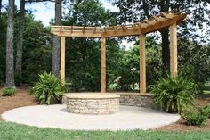 a stone fire pit in the middle of a yard with trees and shrubs around it